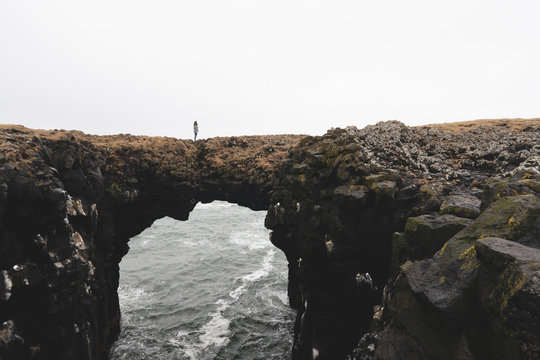 Iceland, Arnarstapi, woman standing on rock arch