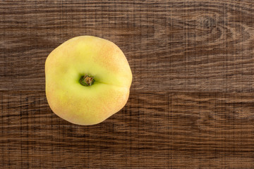 One fresh ripe Saturn peach top view on brown wood background.
