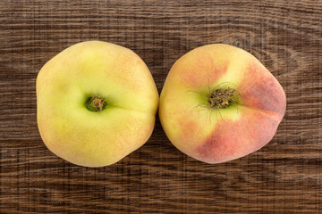 Two fresh ripe Saturn peaches flatlay on brown wood background.
