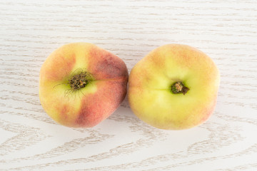 Two fresh ripe Saturn peaches flatlay on grey wood background.