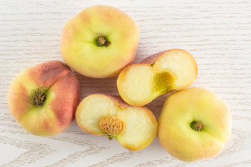 Three fresh ripe Saturn peaches and one cut in two halves top view on grey wood background.