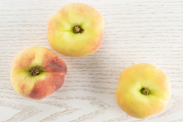 Three fresh ripe Saturn peaches top view on grey wood background.