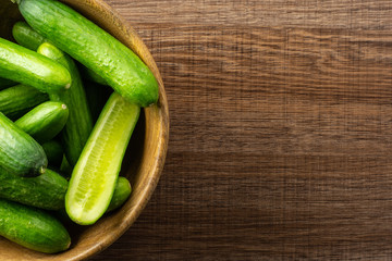 Fresh mini cucumbers in a wooden bowl on brown wood background.