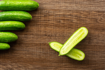Five fresh mini cucumbers and one cut in two halves flatlay on brown wood background.