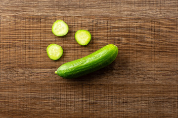 One fresh mini cucumber and three round slices flatlay on brown wood background.