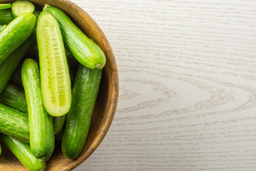 Fresh mini cucumbers in a wooden bowl on grey wood background.