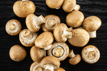 Fresh raw brown champignons flatlay on black wood background.
