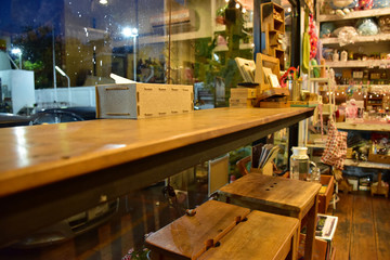 A counter bar made from wood is in the coffee cafe in the evening. There are mini decor on the counter and shelf.