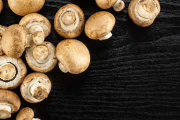 Fresh raw brown champignons table top on black wood background.