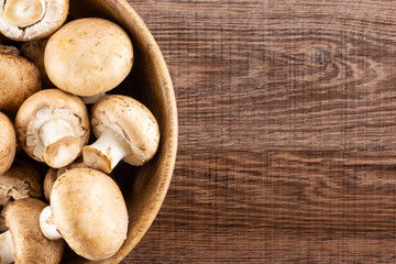 Fresh brown champignons in a wooden bowl top view on brown wood background raw mushrooms.