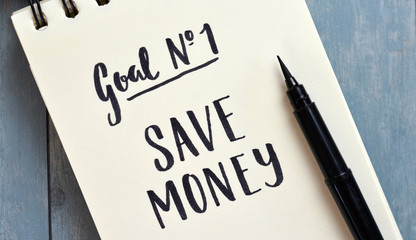 GOAL #1 SAVE MONEY hand-lettered in notebook on blue wooden desk with pen