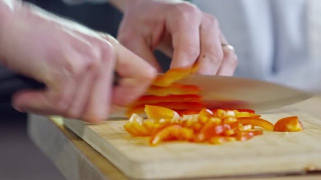 Close up hands of unrecognizable cook using knife when chopping red bell peppers on cutting board