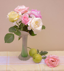 The bouquet of roses in pastel colors in a vase with apples on table, still life