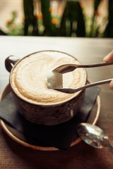 Close-up of adding cube of sugar into coffee cup on wooden table.