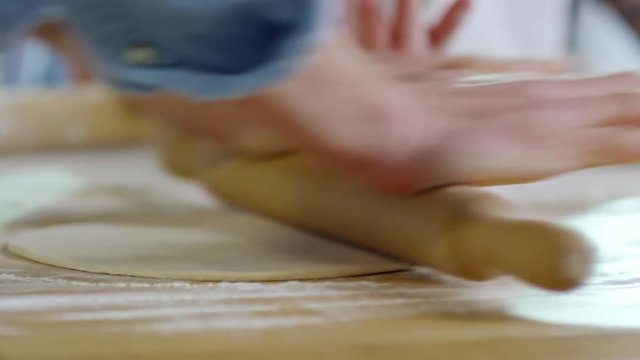 Close up hands of unrecognizable chef rolling out dough on floured wooden surface when baking food with children