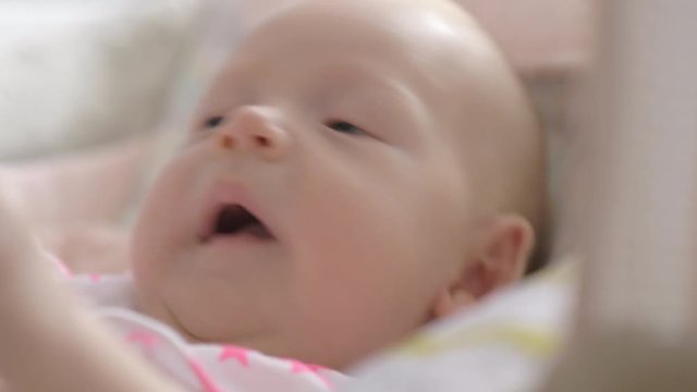Close-up shot of active blue-eyed baby girl of two month old lying in bouncy seat at home