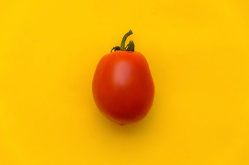 One bright juicy red tomato on a yellow background.