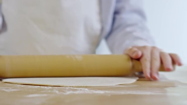 Tracking shot of unrecognizable child rolling out dough on floured wooden surface in cooking class, close up