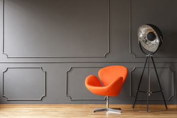 Orange armchair next to lamp in minimal living room interior with wall with molding. Real photo