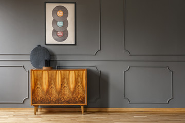 Records on grey wall with molding above wooden cabinet in vintage living room interior. Real photo