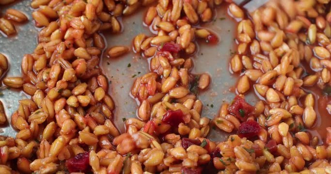 Video of stirring then taking a forkful of cooked farro with beets and spinach and seasonings in a pan.