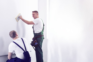 Smiling painter and helper cleaning white wall before painting