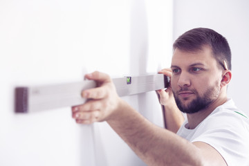 Handyman with bubble level preparing white wall for remodeling