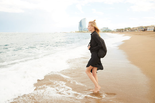 A blonde girl is stepping inside the Mediterranean sea enjoying the water, waves and drops in Barcelona