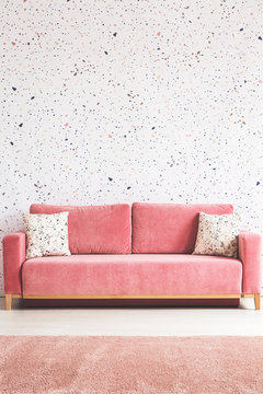 Patterned cushions on pink sofa in living room interior with carpet and wallpaper. Real photo