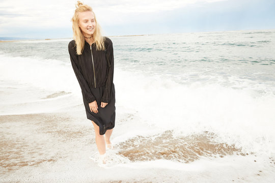 A blonde girl is stepping inside the Mediterranean sea enjoying the water, waves and drops in Barcelona