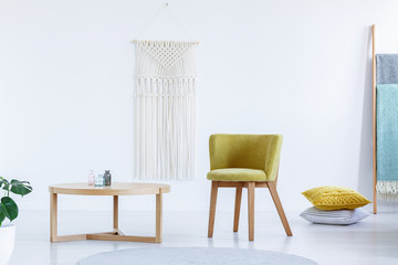 Real photo of a yellow chair standing next to a wooden table in bright, simple living room interior...