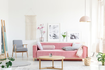 Real photo of a pink couch with pillows standing behind a table, next to an armchair, in front of a...