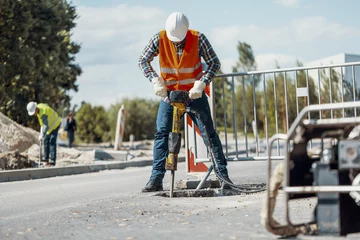 Fotobehang Worker in reflective vest with drill repairing street during roadworks © Photographee.eu