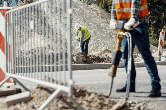 Craftsman in helmetn and vest with shovel working on the street during roadworks