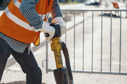 Close-up of worker with white gloves and orange reflective vest using drill during roadworks