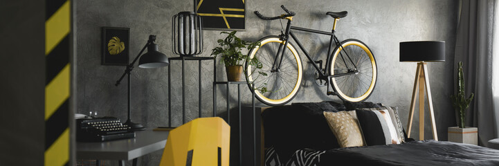 Dark apartment interior with vintage typewriter on desk, double bed with black bedclothes, bike...