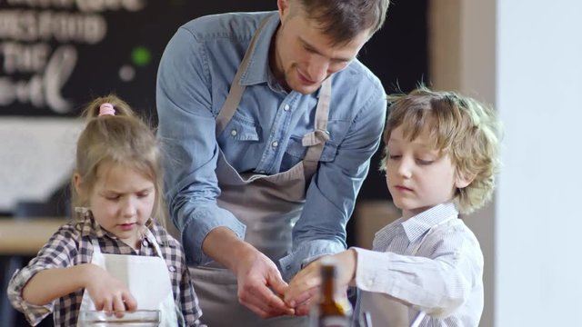 Young father and two children in aprons topping pizza with olives and sweet peppers when cooking together in kitchen