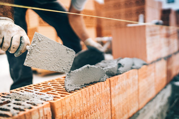 Close up of construction worker details, protective gear and trowel with mortar building brick walls