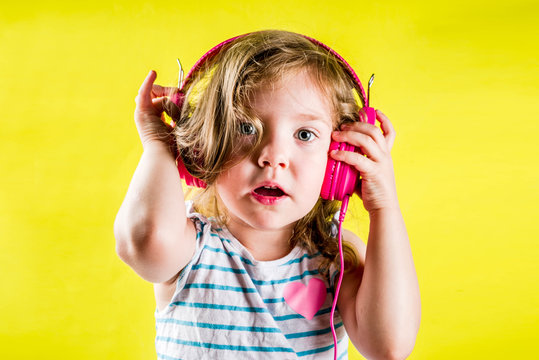 Funny Cute Blonde Toddler Girl Listen Music With Bright Pink Headphones, Yellow Background Copy Space