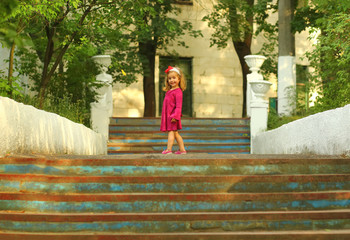 Sunlit portrait of a cute toddler girl posing on old blue stairs