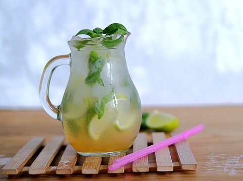 Cold summer drink, lemonade with lime and basil on the basis of sparkling water and sugar syrup in a small glass jug. Served with ice. Summer concept.