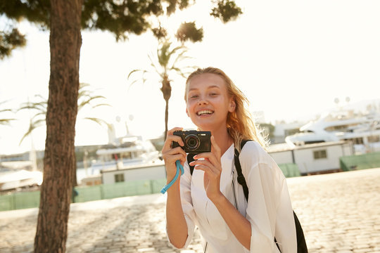 A girl taking a photo with a little camera in Barcelona in front of palms