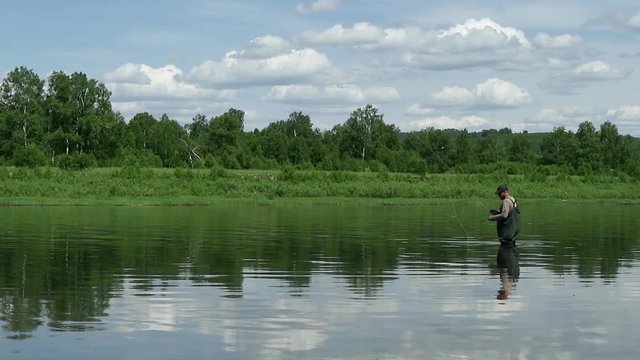 Joyful fisherman is fishing in calm river water near the shore