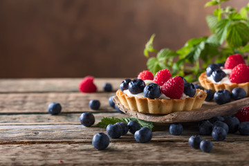  Dessert tarts with raspberries and blueberries on a wooden table.
