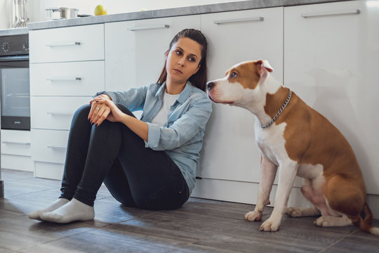 Sad woman sitting on a kitchen floor with her dog