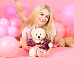 Fototapeta na wymiar Young woman on bed hugging teddy bear. Birthday girl concept. Blonde on smiling face relaxing with teddy bear toy. Woman cute celebrate birthday with balloons. Girl in pajama, pink background.