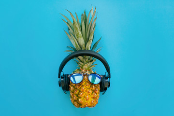 stylish pineapple in sunglasses and headphones on trendy blue paper background. summer flat lay. vacation and party concept. space for text. hipster holidays