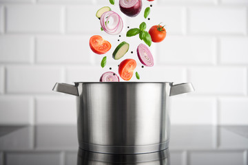 Healthy eating. Stainless steel pot with vegetables on the induction stove with white metro tiles...