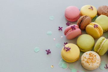 colorful macarons on trendy pastel gray paper with lilac flowers and confetti. tasty pink, yellow, green and brown macaroons. candy bar for party. food photography. yummy background