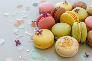 colorful macarons on trendy pastel gray paper with lilac flowers and confetti. tasty pink, yellow, green and brown macaroons. candy bar for party. food photography. yummy background